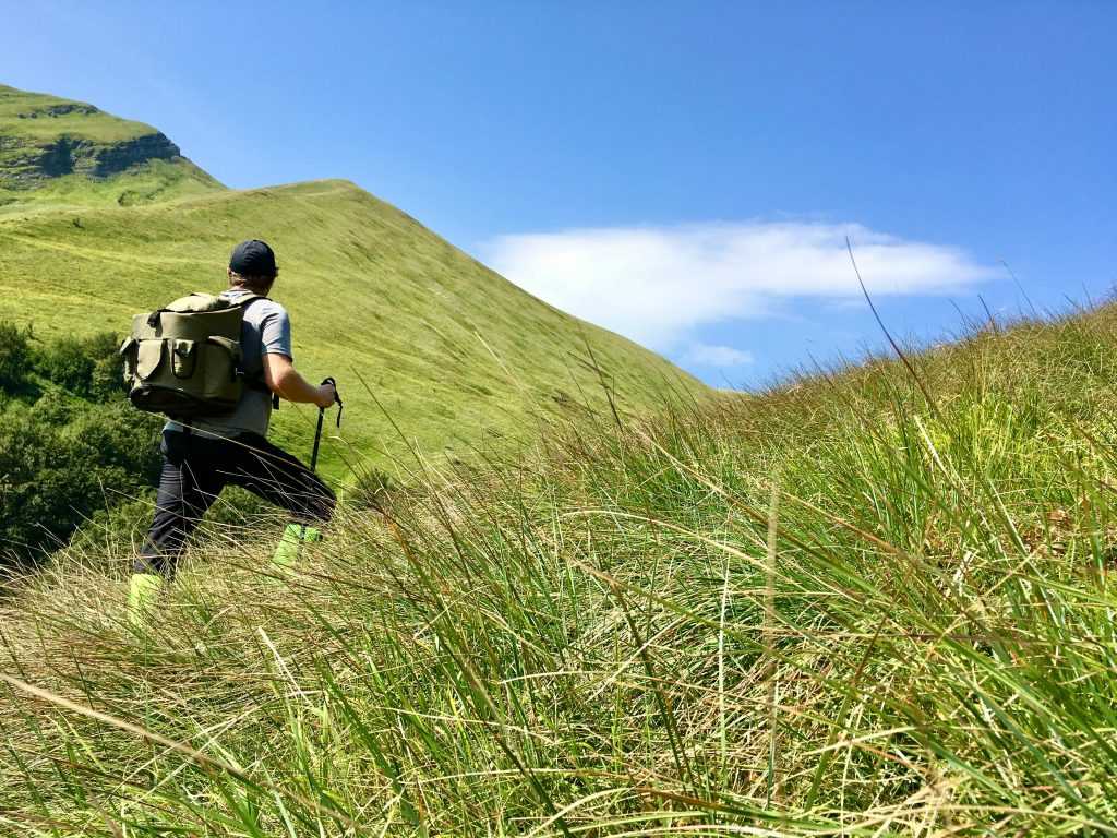 A hiker trekking through lush green hills under a clear blue sky in Italy.